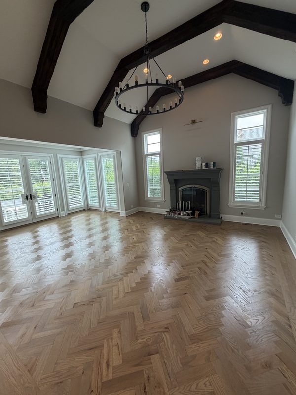 Red oak herringbone hardwood floor installed in a vaulted great room with exposed beams and a stone fireplace