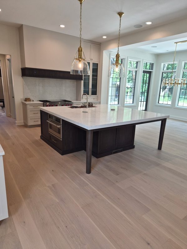Remodeled kitchen with a dark oak island, quartz countertop, brass pendants and white oak plank flooring
