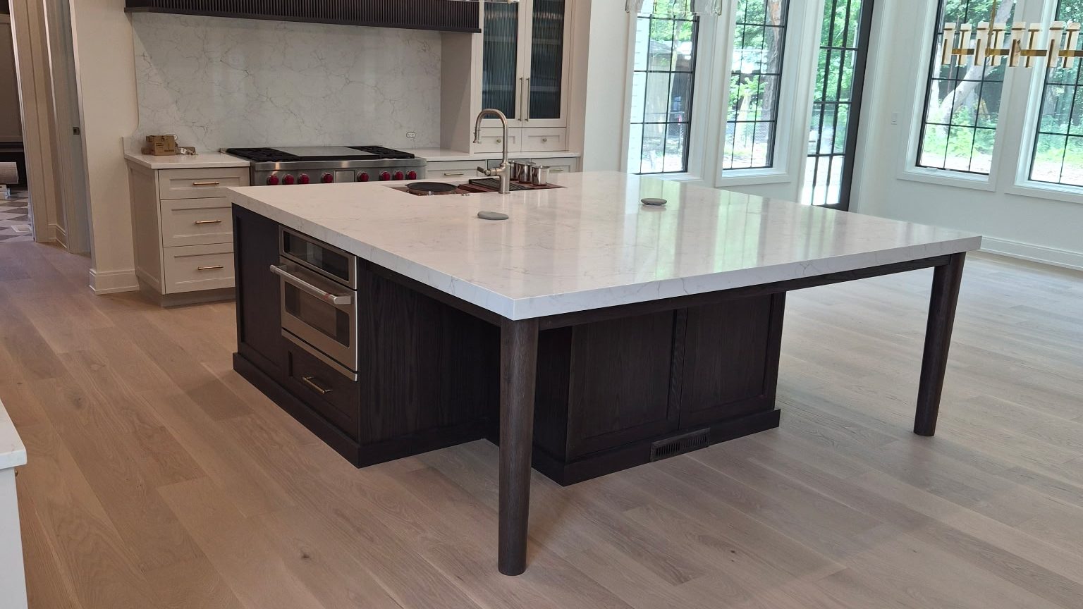 Remodeled kitchen with a dark oak island, quartz countertop, brass pendants and white oak plank flooring