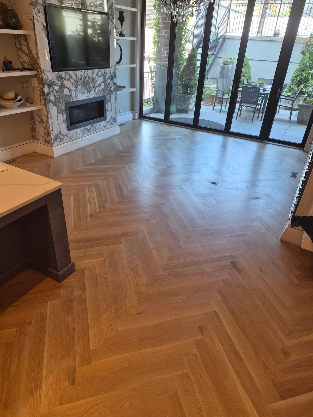 Light white oak herringbone floor in a living room with a marble fireplace surround and black steel doors