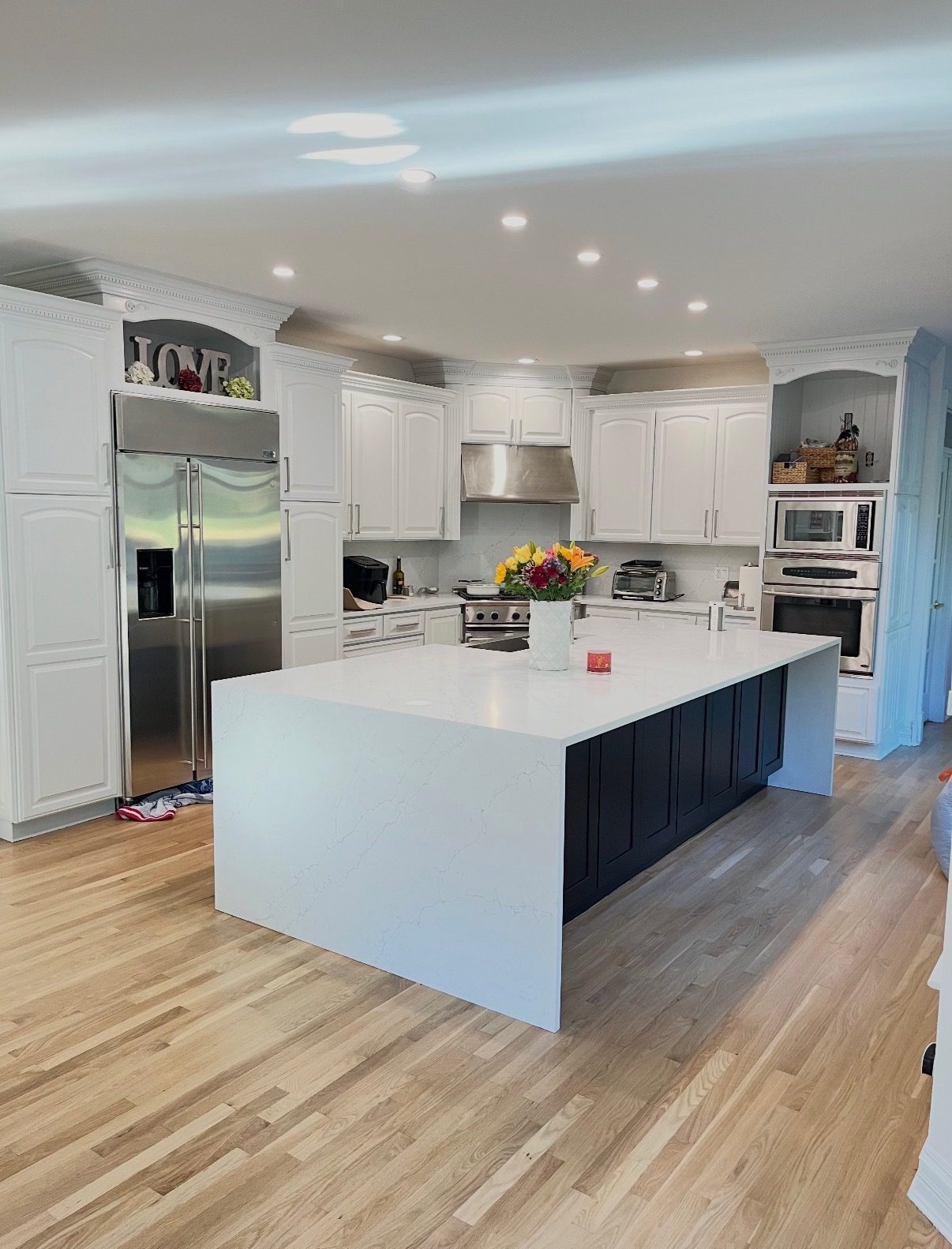 White quartz countertops and a navy island in a remodeled kitchen with light hardwood floors